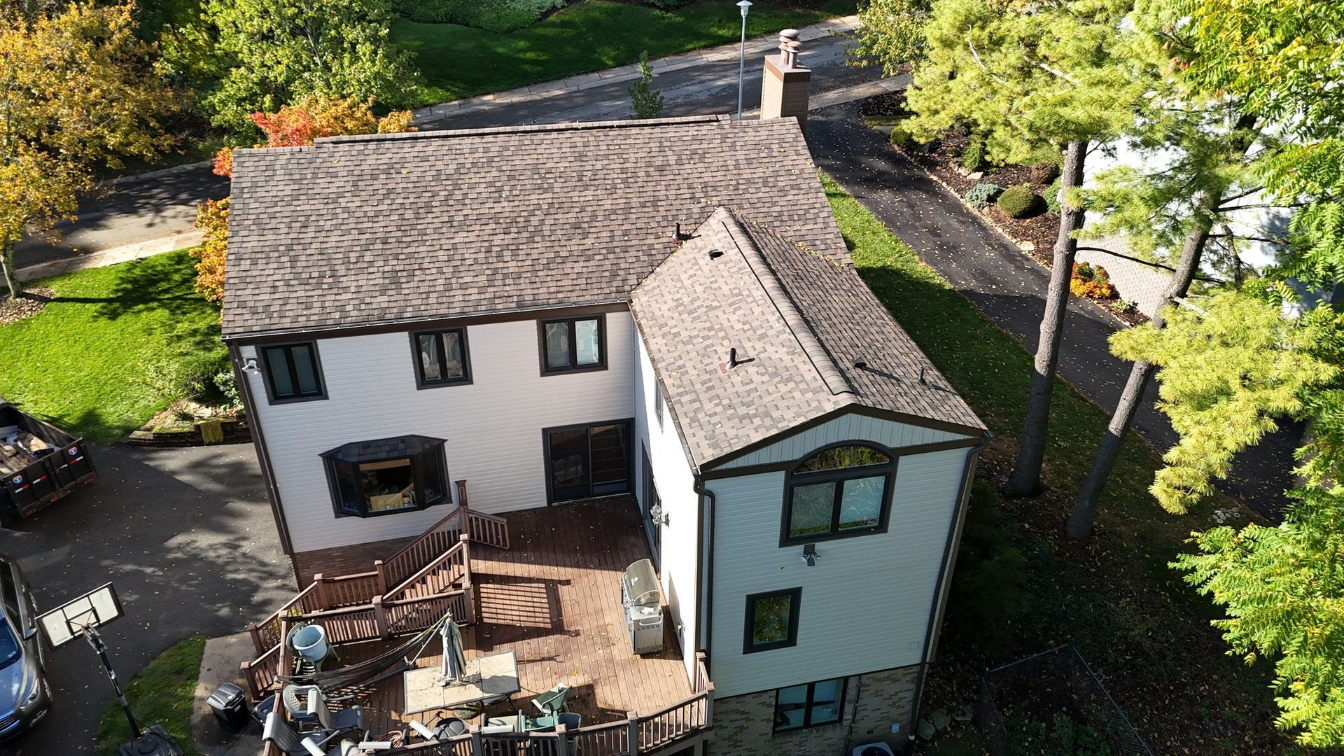 Two-story house with a brown shingle roof, surrounded by trees and a green lawn.