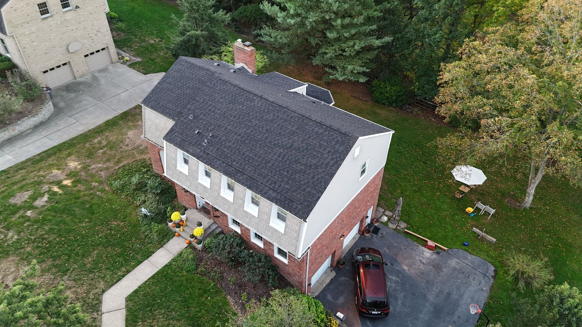 An aerial view of a two-story brick and siding house with a dark gray roof. A black car sits in the driveway.