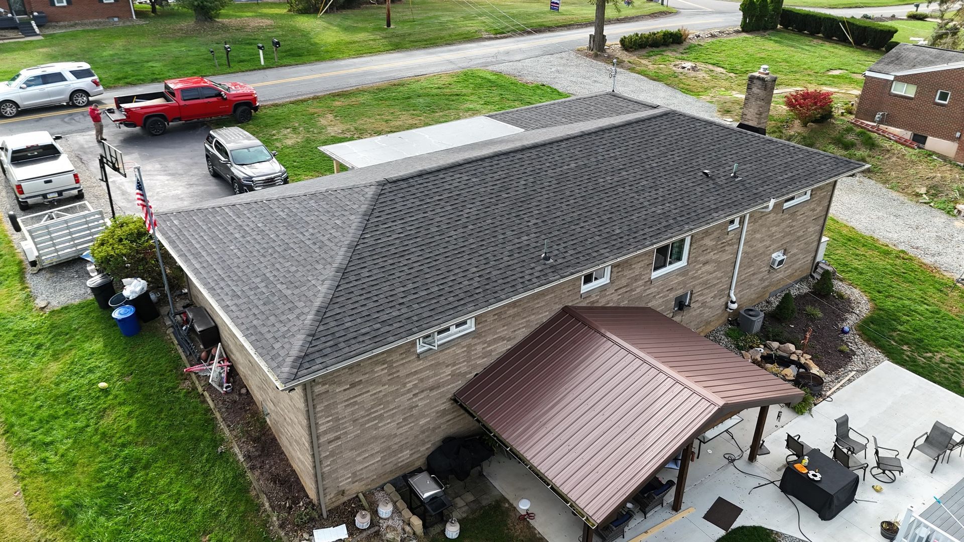 Overhead view of a brick house with a dark gray shingled roof, brown metal porch roof, and vehicles in the driveway.