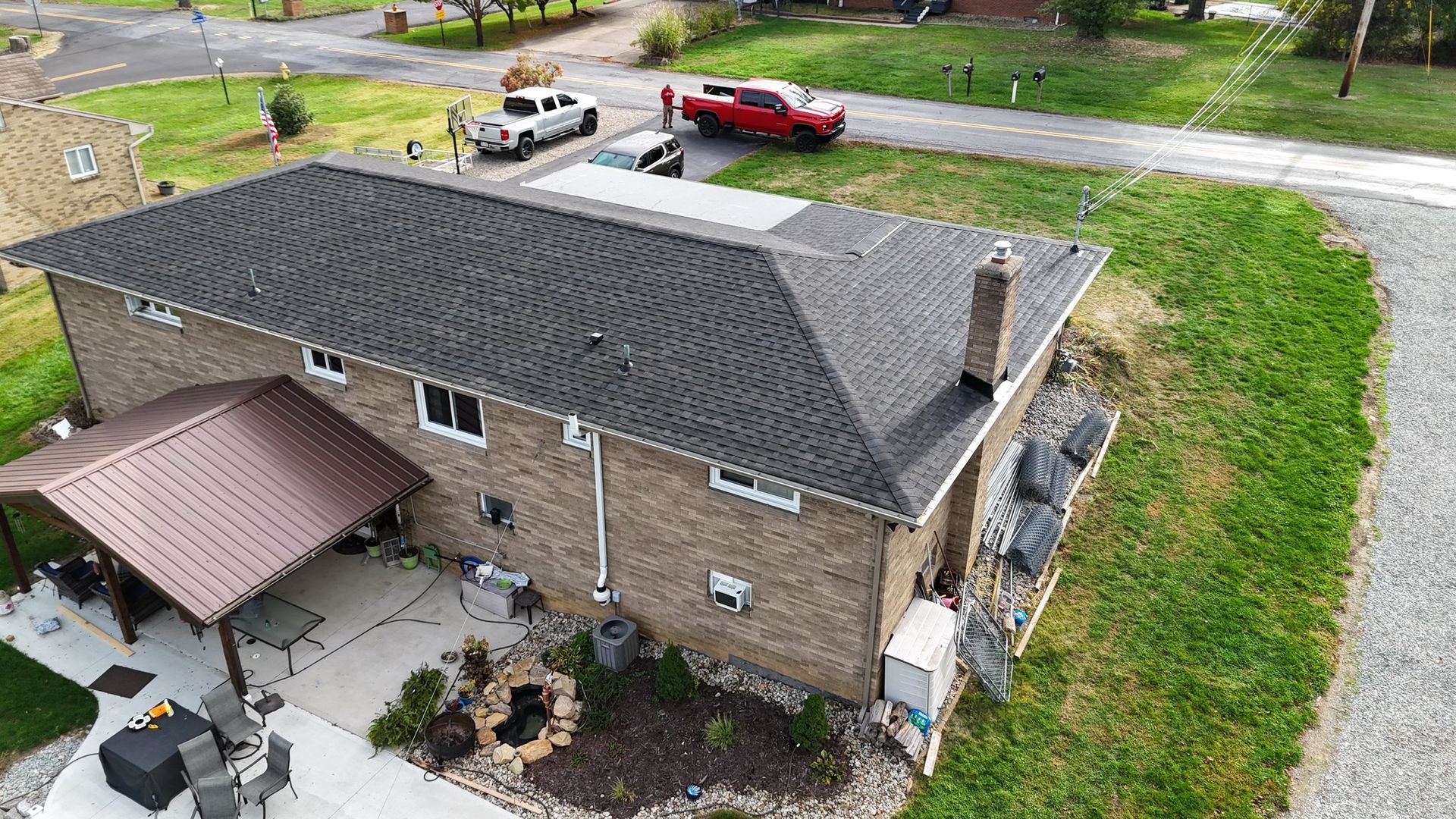 Aerial view of a two-story brick house with dark gray roof, red car, and white truck parked on the driveway.