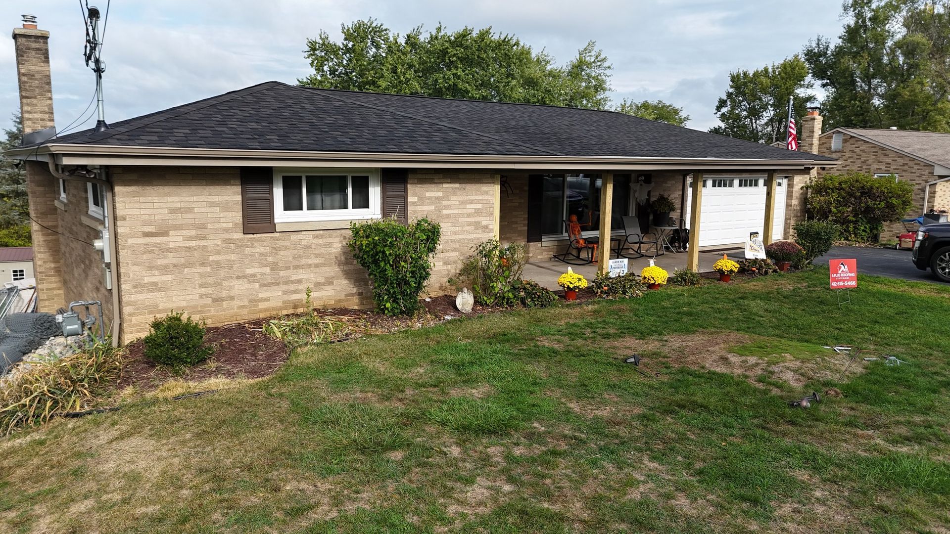 Brick ranch house with black roof, brown shutters, and front porch. Green grass and flowers in the yard.