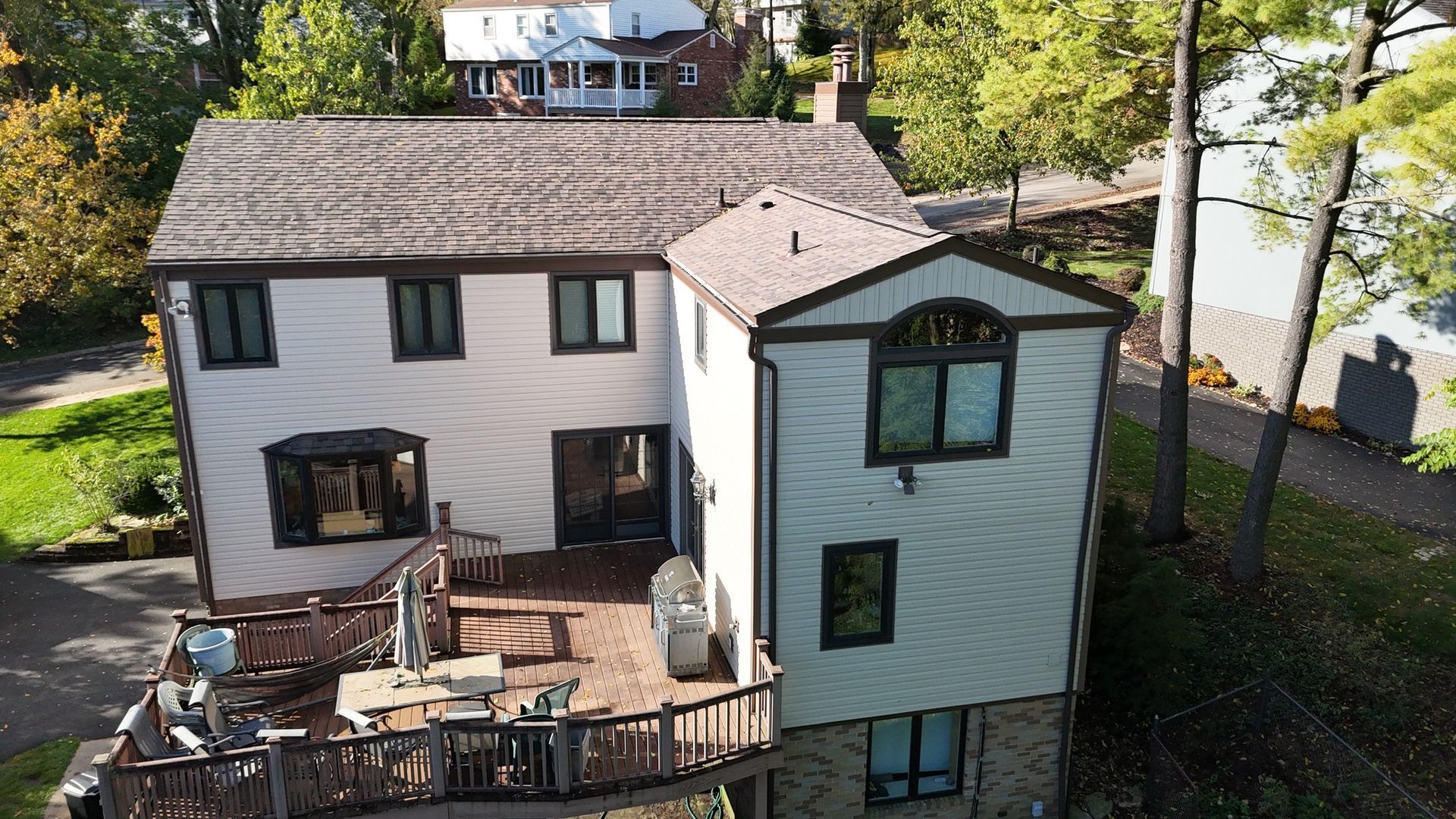 Two-story house with a brown roof and a deck, surrounded by trees.