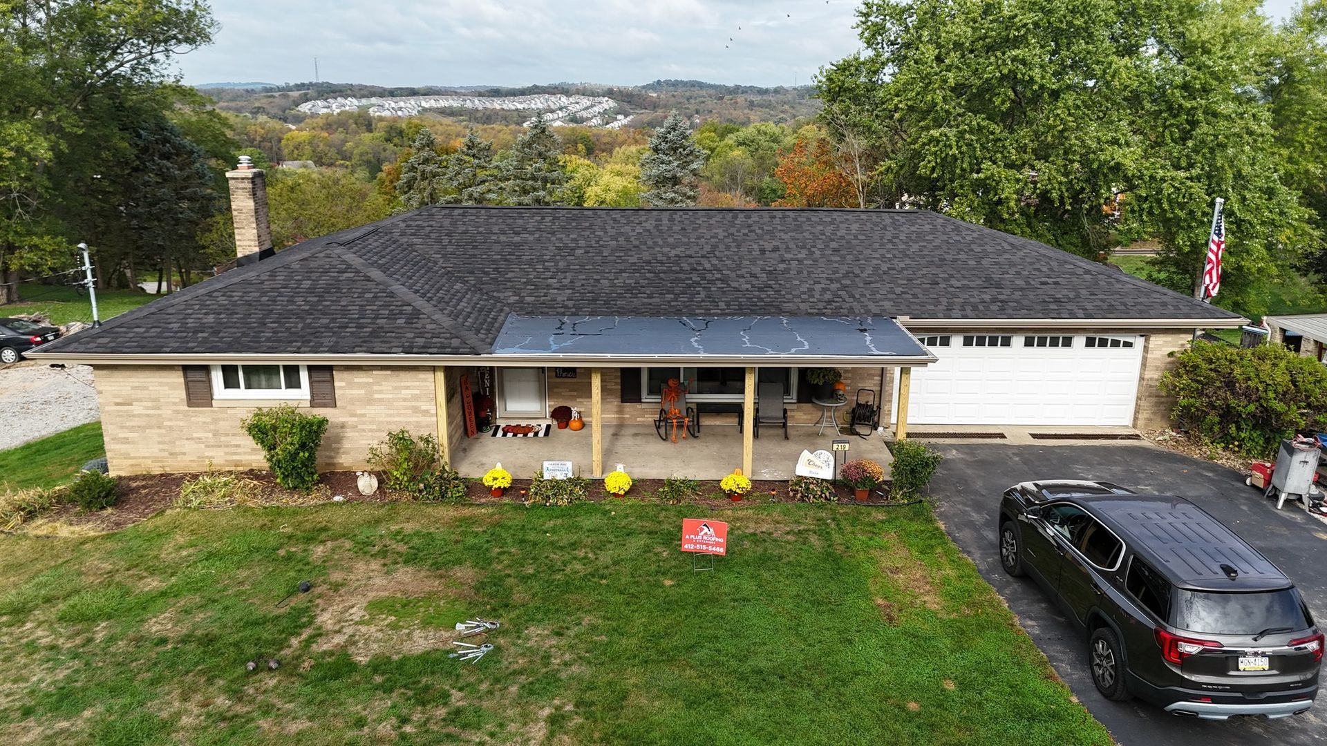 A single-story brick house with a dark roof and a porch. A black SUV sits in the driveway, and pumpkins decorate the lawn.