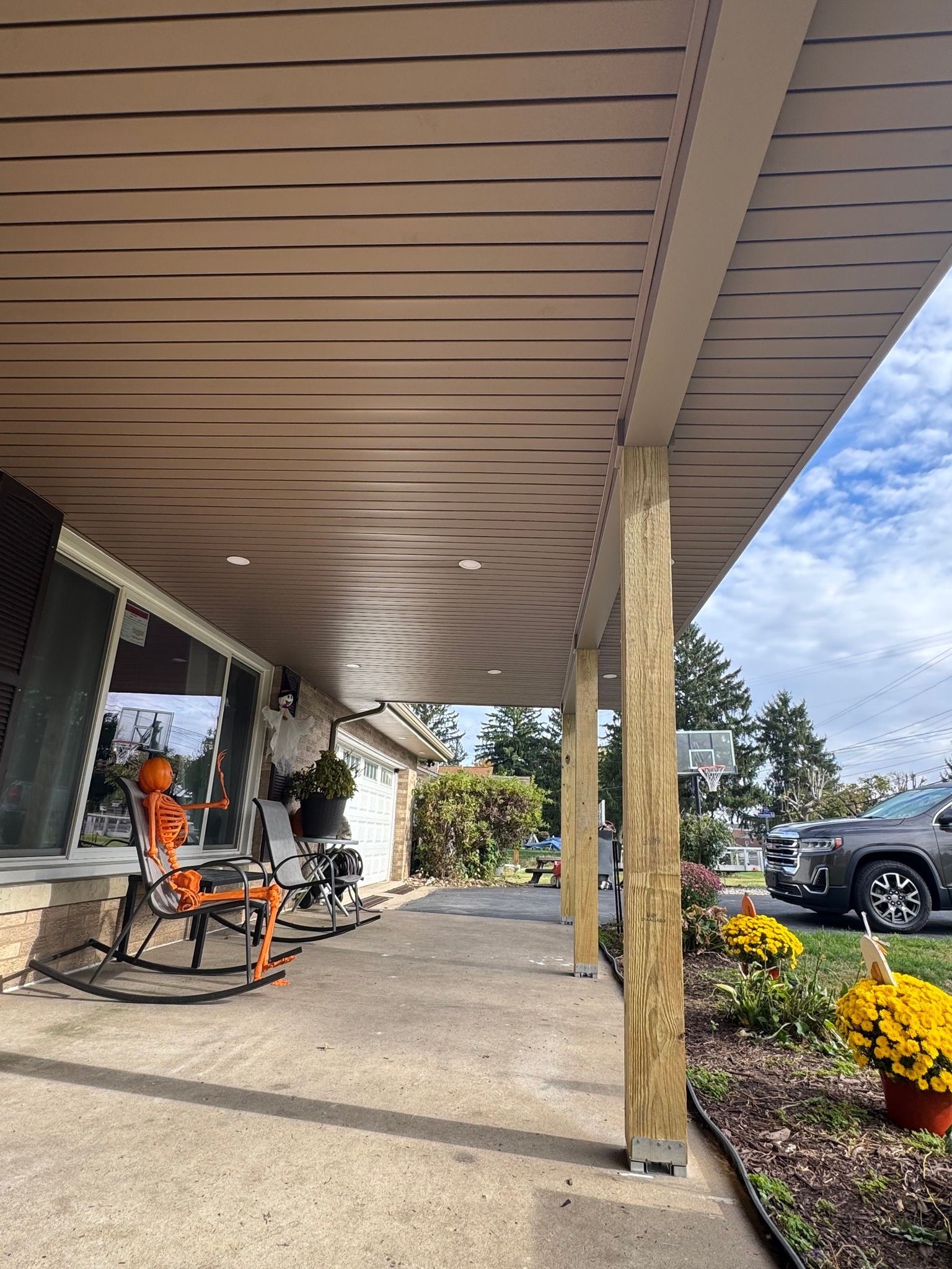 Covered porch with concrete floor, decorated for fall. Pumpkins, flowers, and a car are visible.