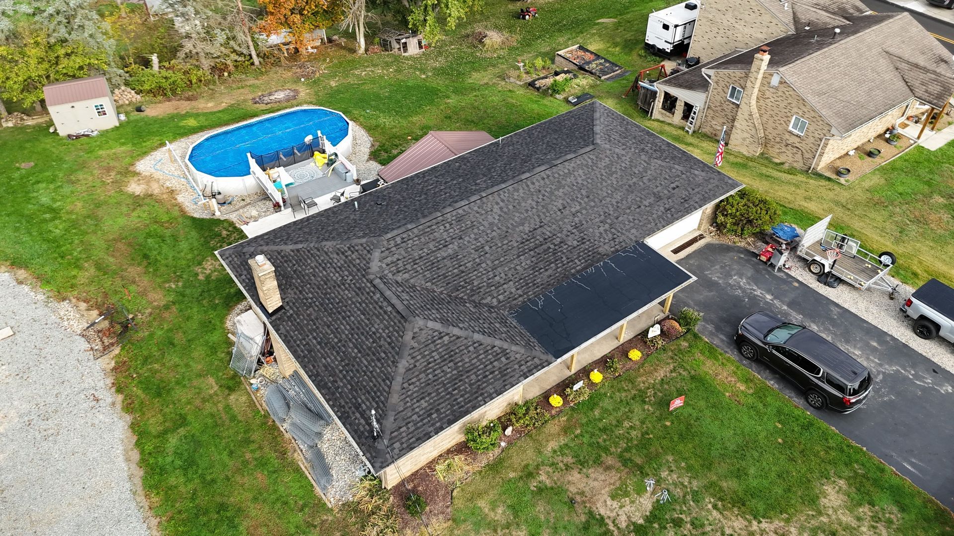 Aerial view of a house with a dark roof, driveway, and an above-ground pool in a grassy yard.