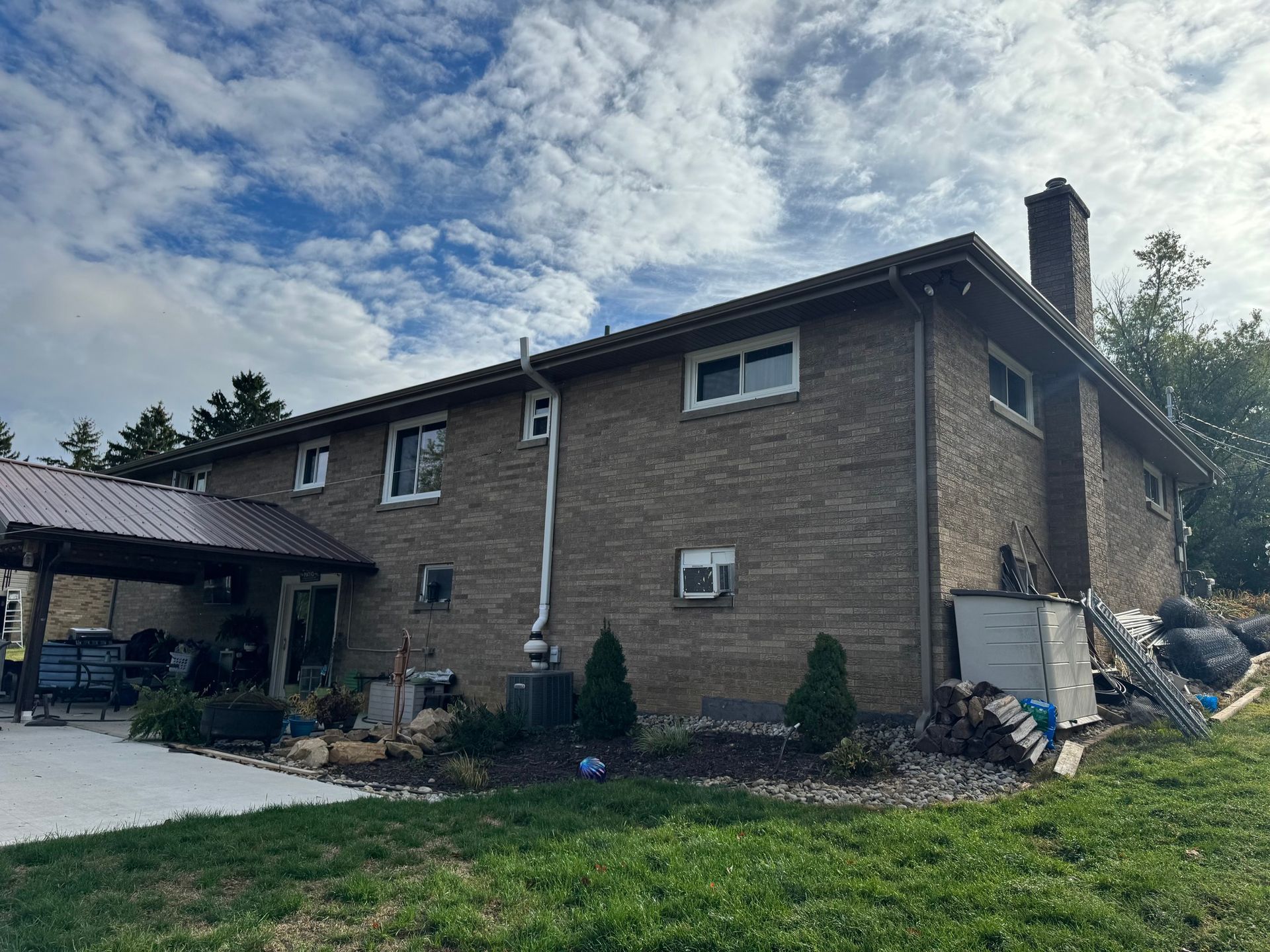 Brick house with a brown metal roof, chimney, and carport on a cloudy day.