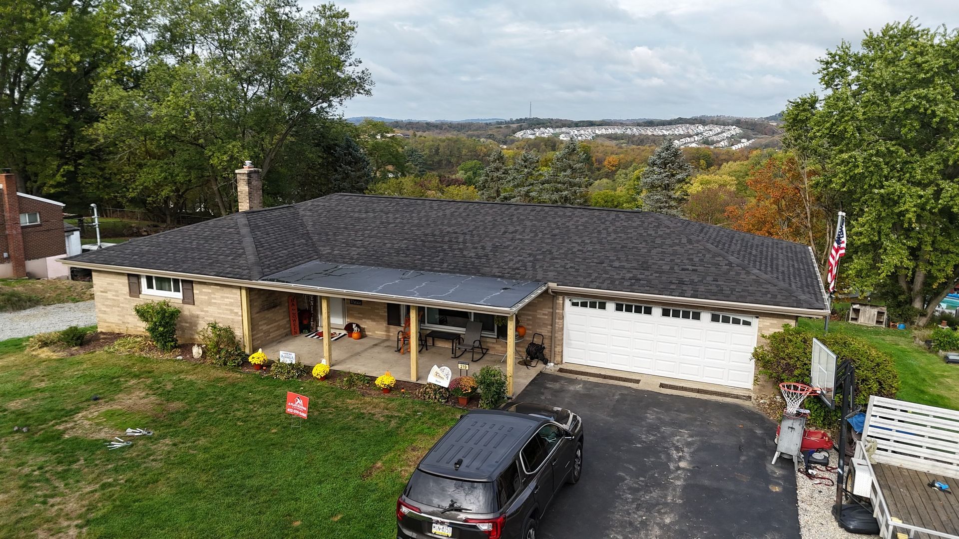 Low-angle view of a brick ranch-style house with a dark roof, driveway, and a black SUV.