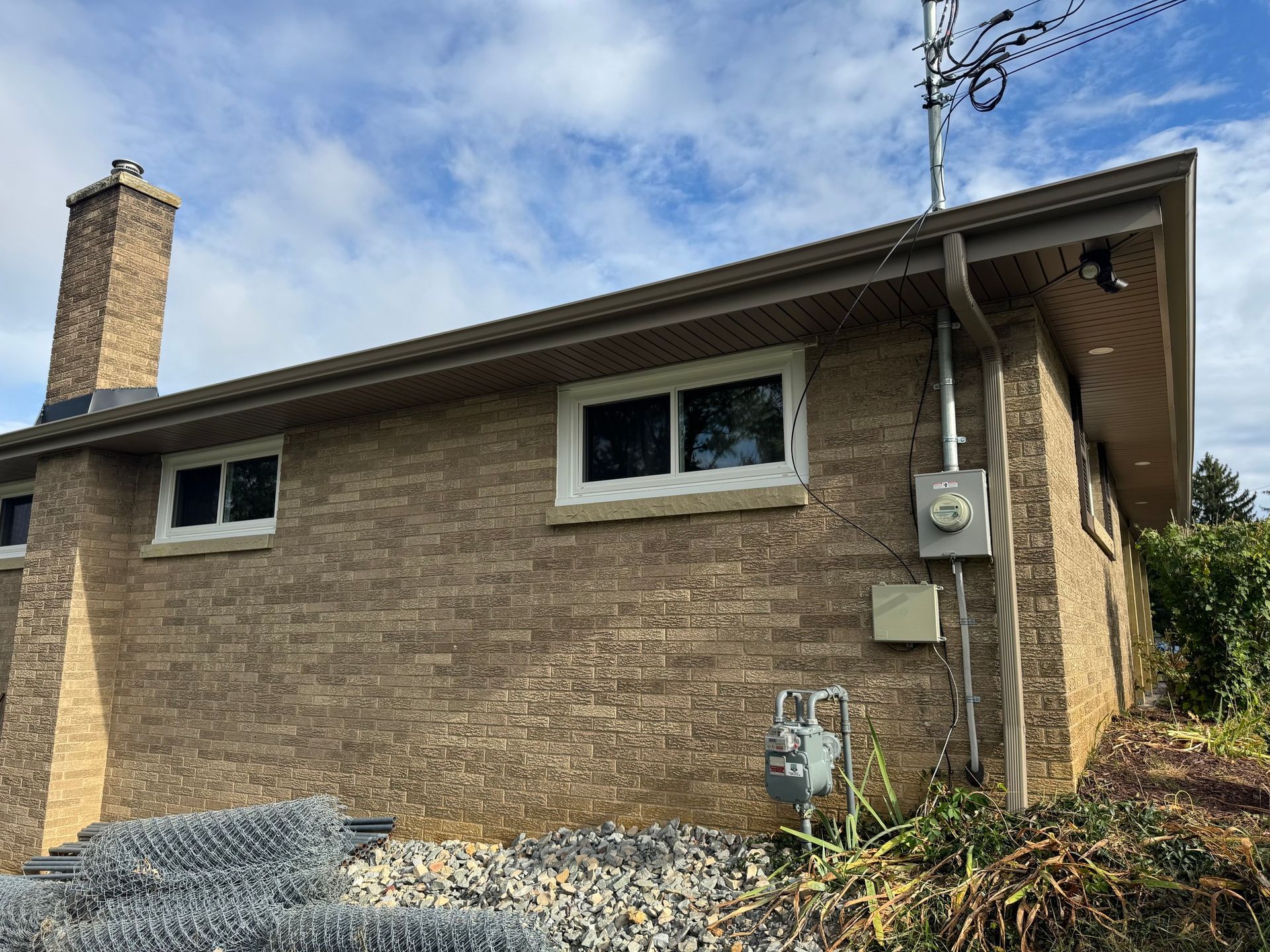 Brick building with white-framed windows, brown gutters, and an outdoor electrical panel; gas meter in foreground.