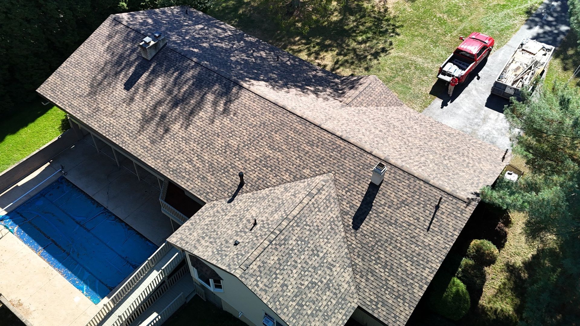 Overhead view of a house with a brown roof, swimming pool, driveway, and a red truck.