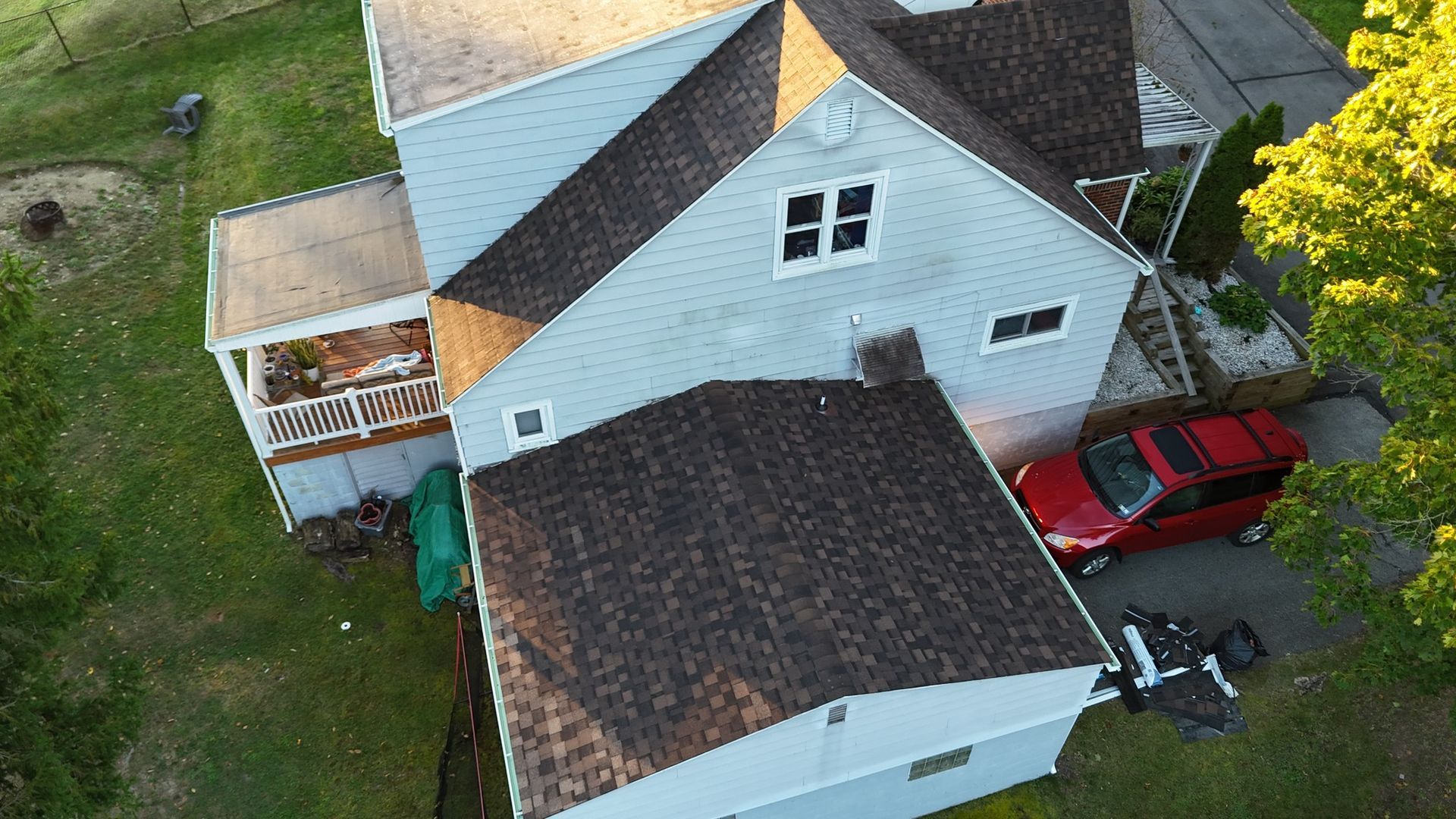 Aerial view of a gray house with a brown roof, a red car, and a green lawn.