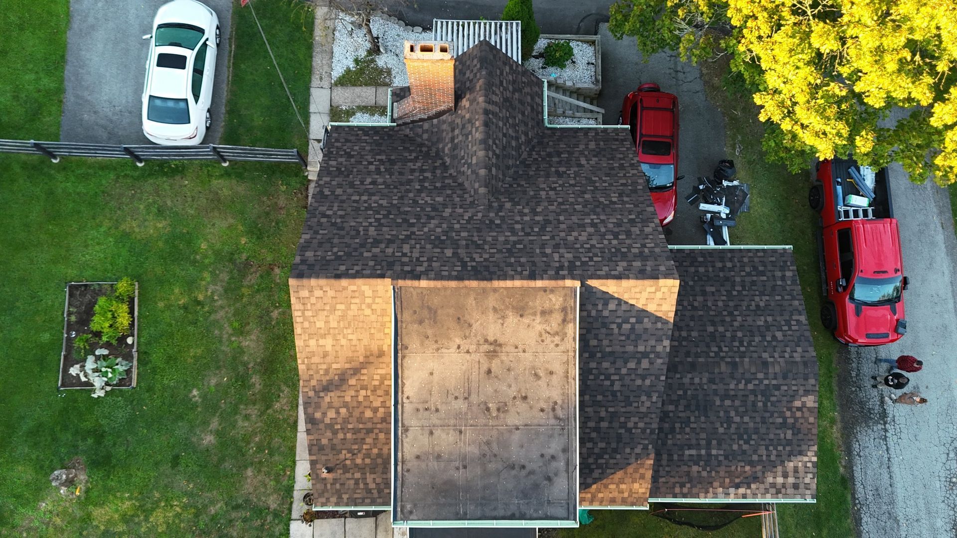 Overhead view of a house with a car parked in the driveway and two fire trucks nearby.