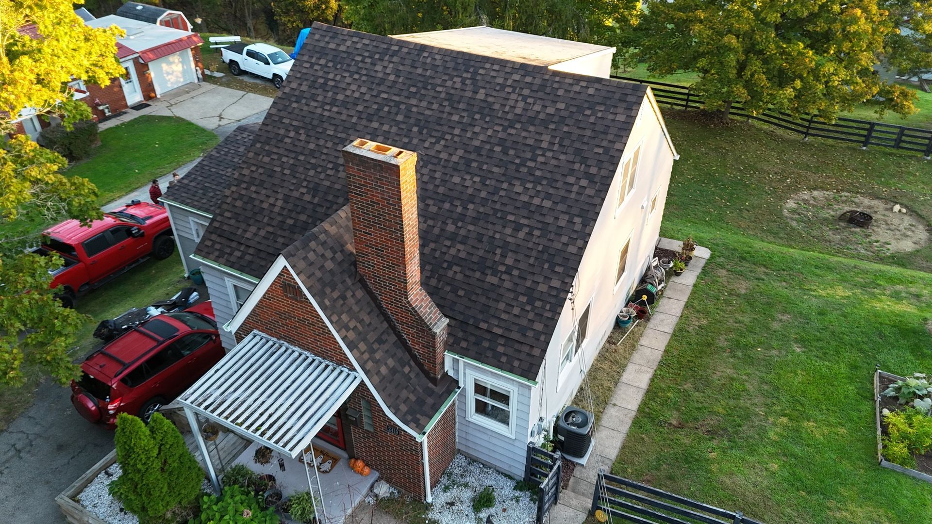 Aerial view of a gray house with a brown roof and chimney, green yard, and a red truck parked beside it.