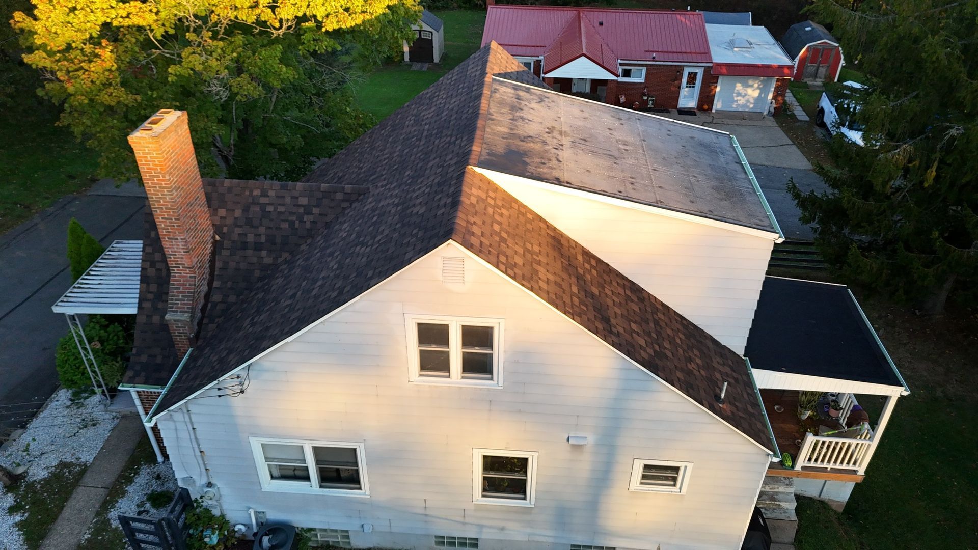 A two-story light blue house with a dark brown roof and a tall brick chimney, viewed from above.