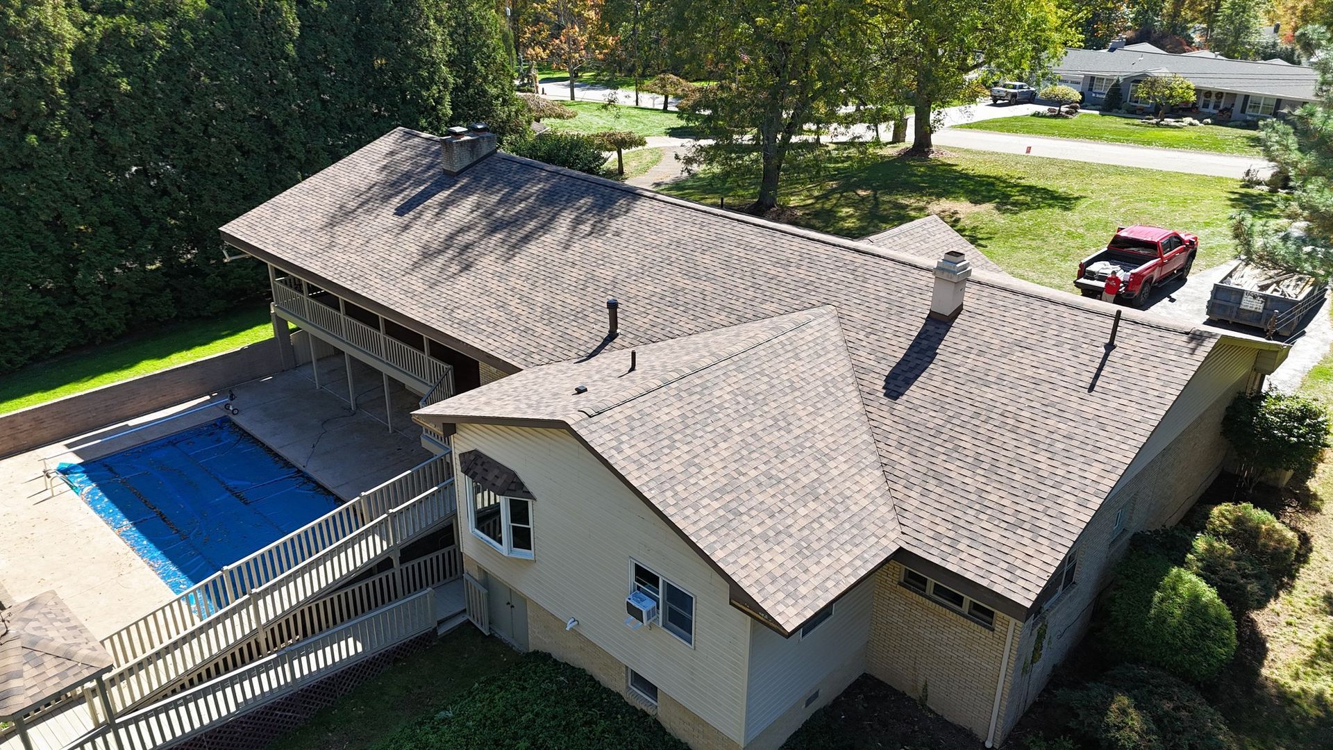 Aerial view of a house with a pool, deck, and car. Brown roof, beige siding, and green lawn.
