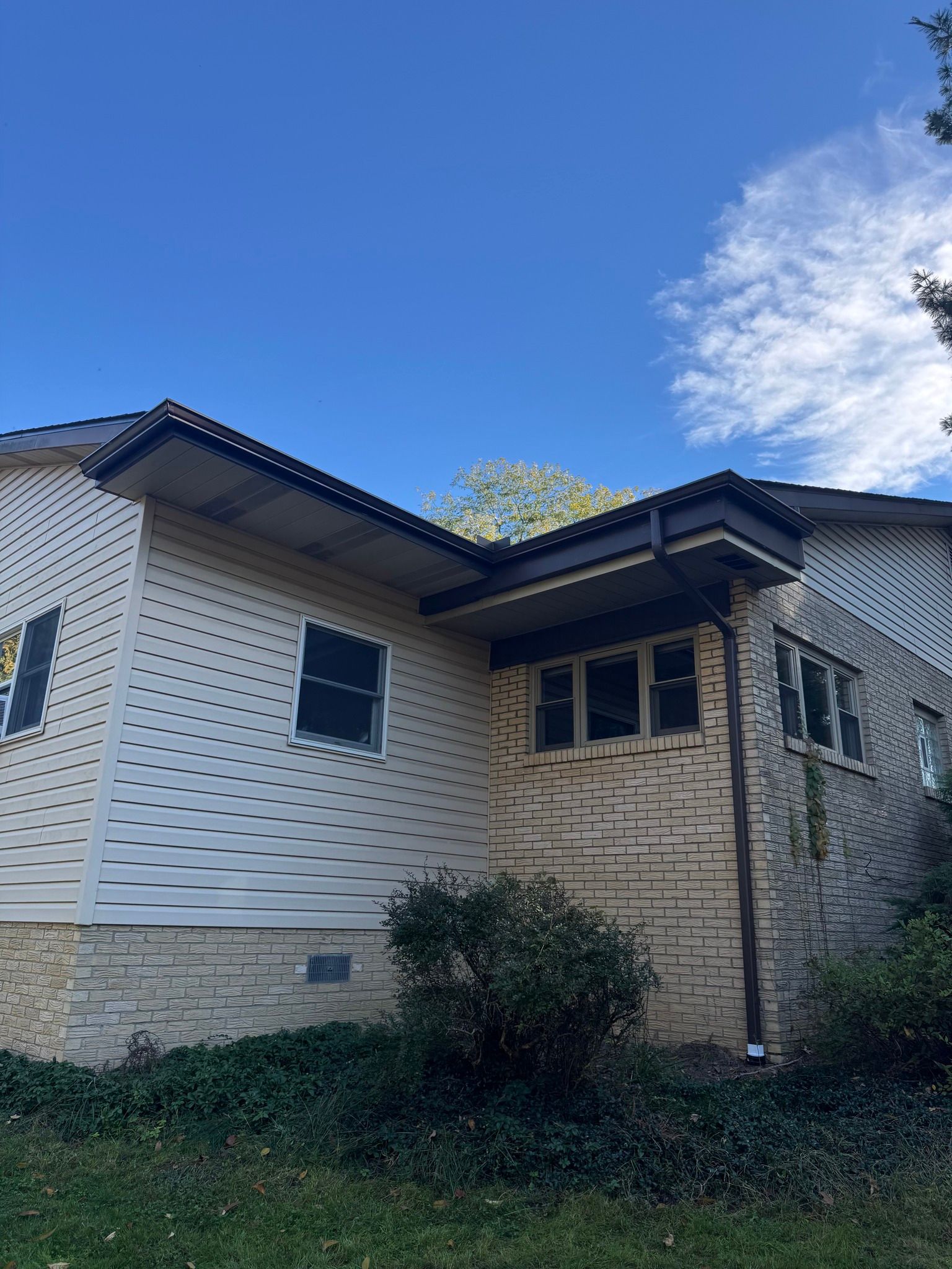 Beige and brick house with dark trim and gutters under a blue sky.