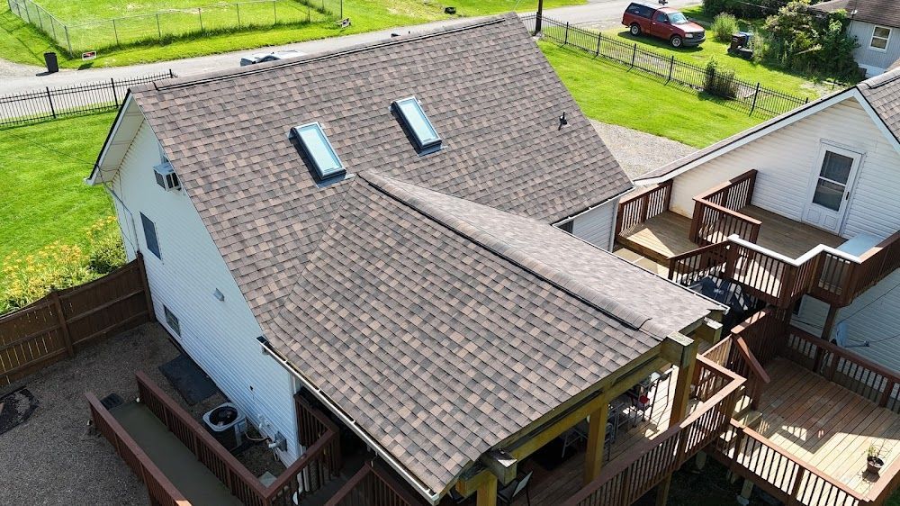 Aerial view of a house with a brown shingled roof, skylights, and attached wooden decks.