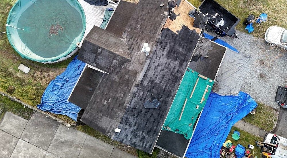 Overhead view of a house with a damaged roof covered in blue and green tarps, with a round pool nearby.