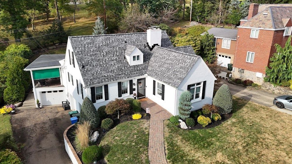 White house with gray roof, brick pathway, green lawn, black shutters, and landscaping.