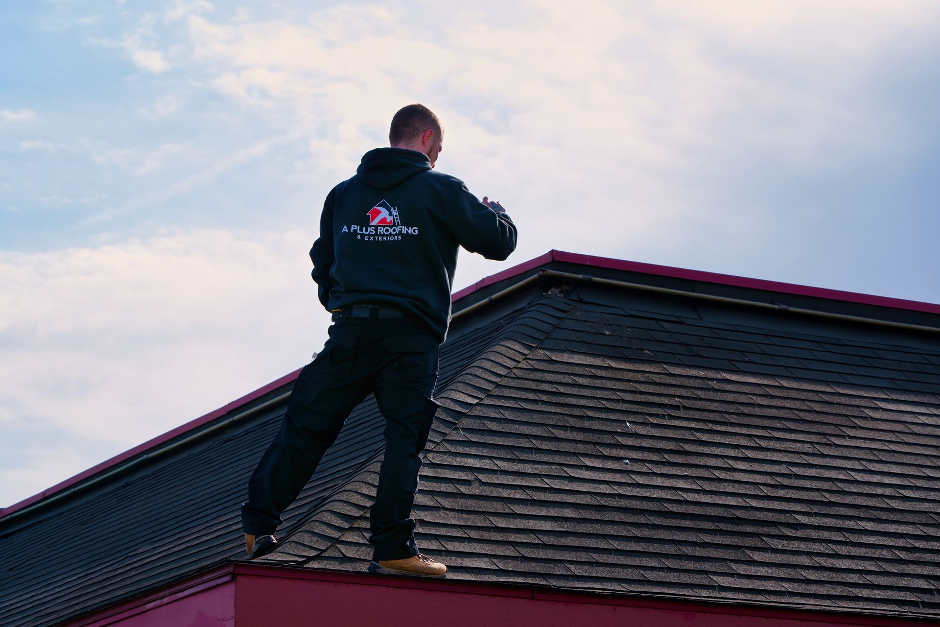 Person in black hoodie on rooftop, checking watch against a blue sky.