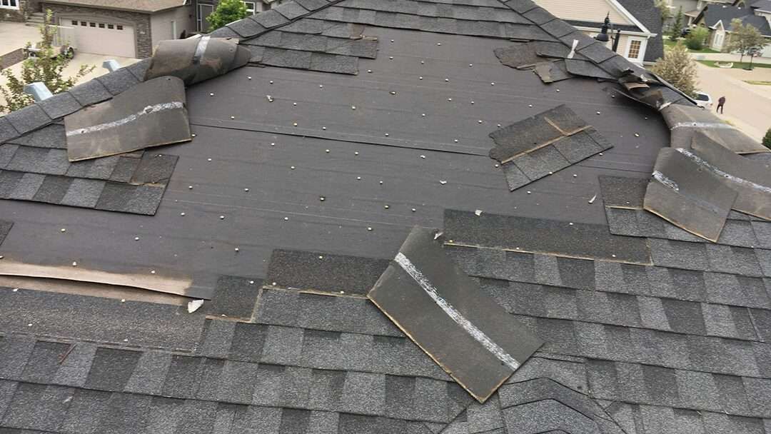 Damaged asphalt shingle roof with missing and dislodged shingles.