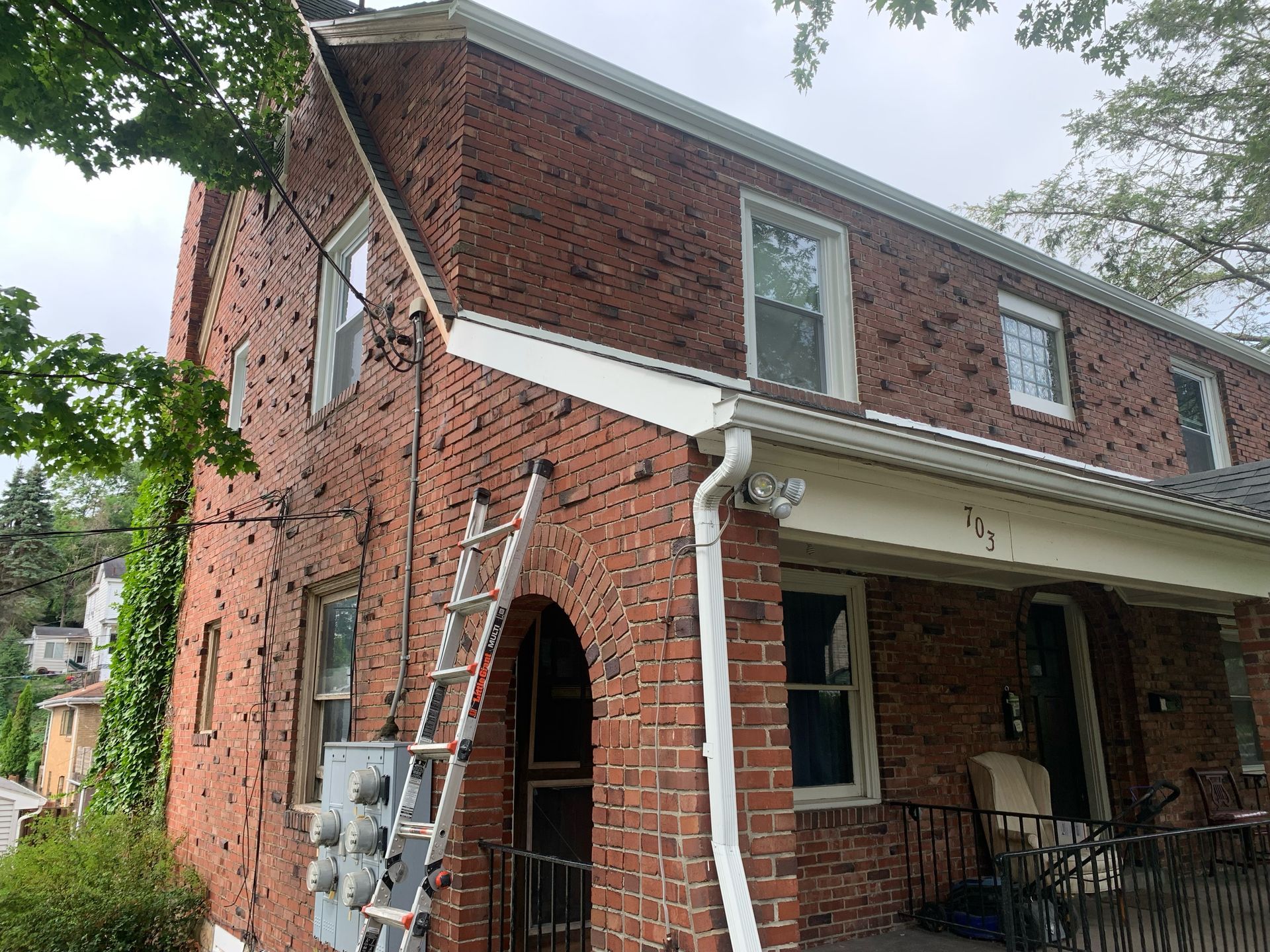 Brick house with white trim, a ladder, and electrical boxes.