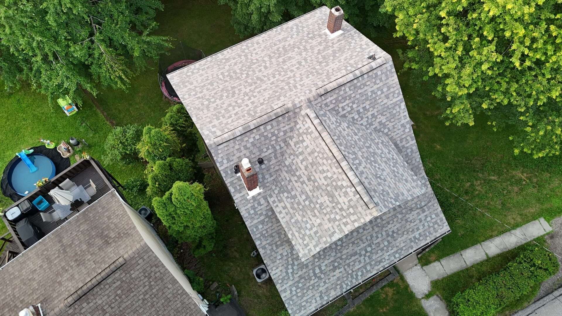 Overhead view of a house with a gray shingle roof, chimney, and surrounding greenery.
