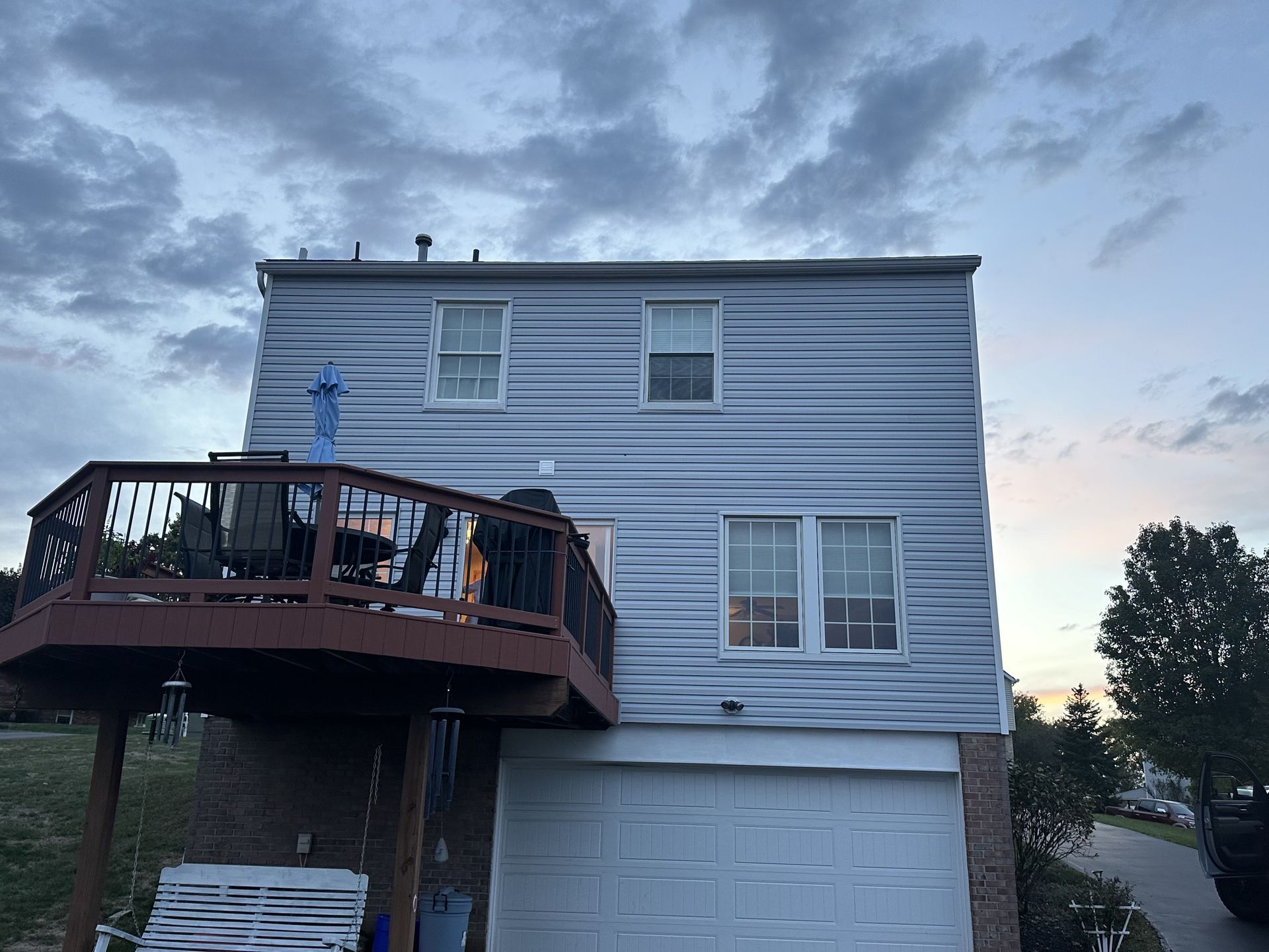 Two-story house with a deck and a garage against a cloudy sky.