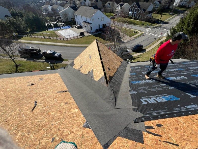Person on a roof installing shingles, residential area in background.