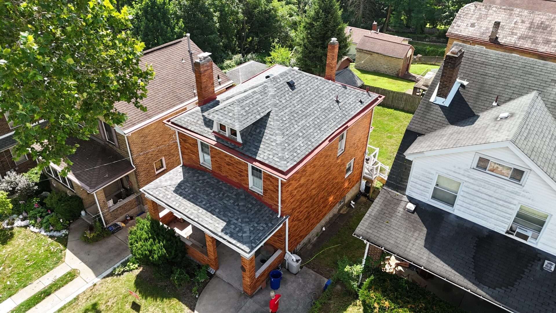Aerial view of brick houses with dark gray roofs, surrounded by trees and grass on a sunny day.