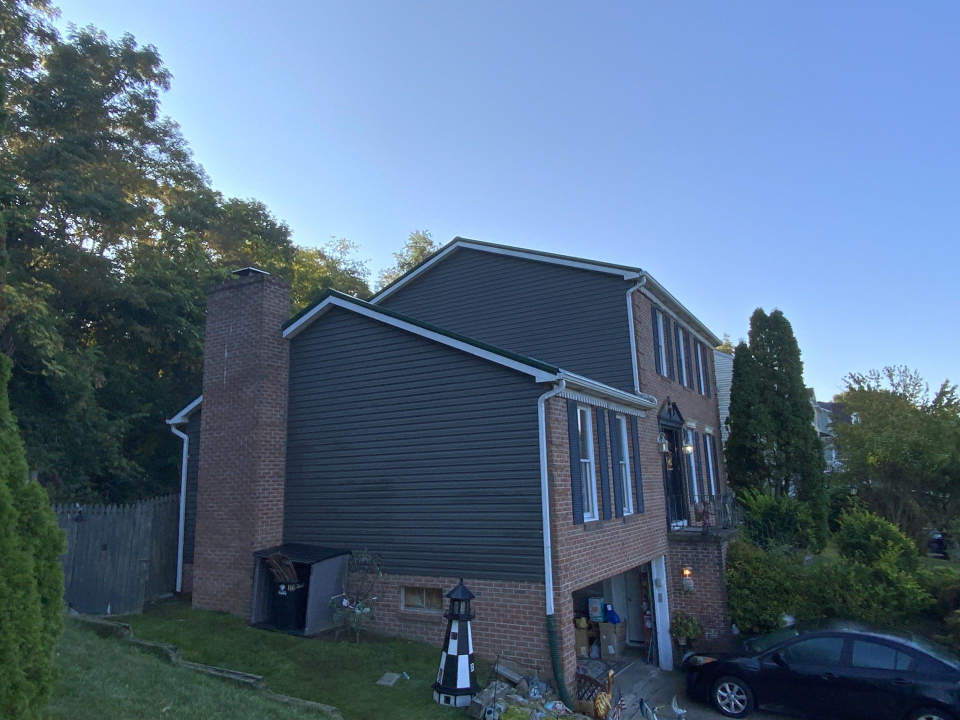 Two-story house with dark gray siding, brick facade, chimney, black car, and a blue sky.