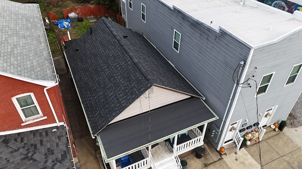 Overhead view of a house with a black roof, next to a gray building and a red building.