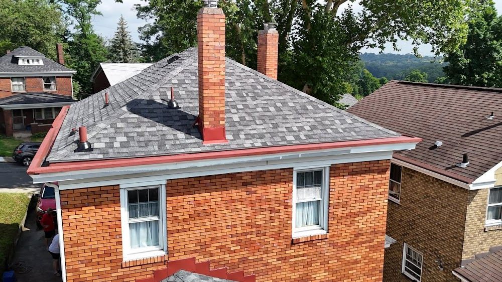 Brick house with gray roof, red trim, two chimneys, and two windows.