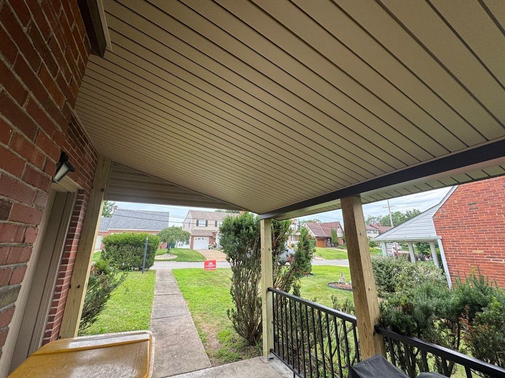 Covered porch with beige ceiling, brick wall, and view of a grassy yard with houses.