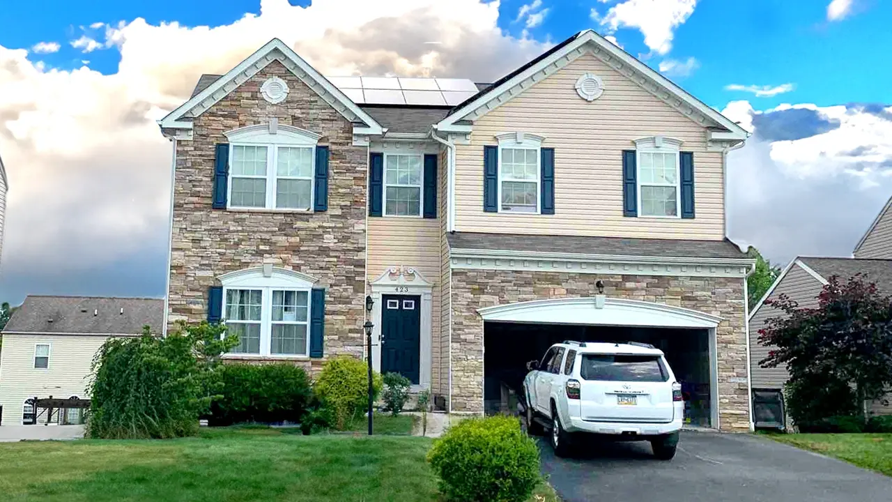 Two-story house with stone facade, tan siding, blue shutters, and a garage with a white SUV.