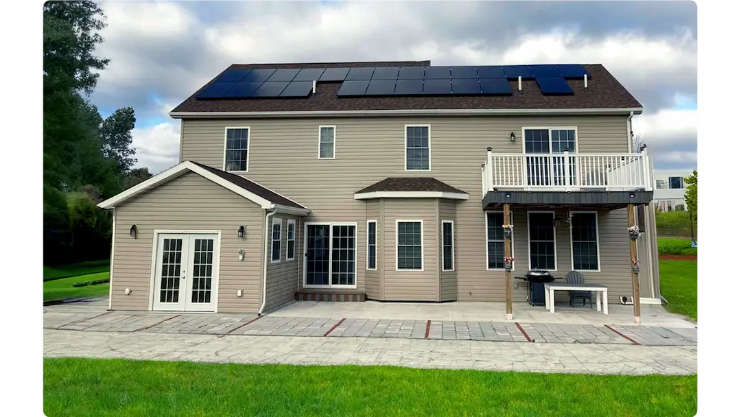 Back view of a two-story beige house with solar panels on the roof and a patio.