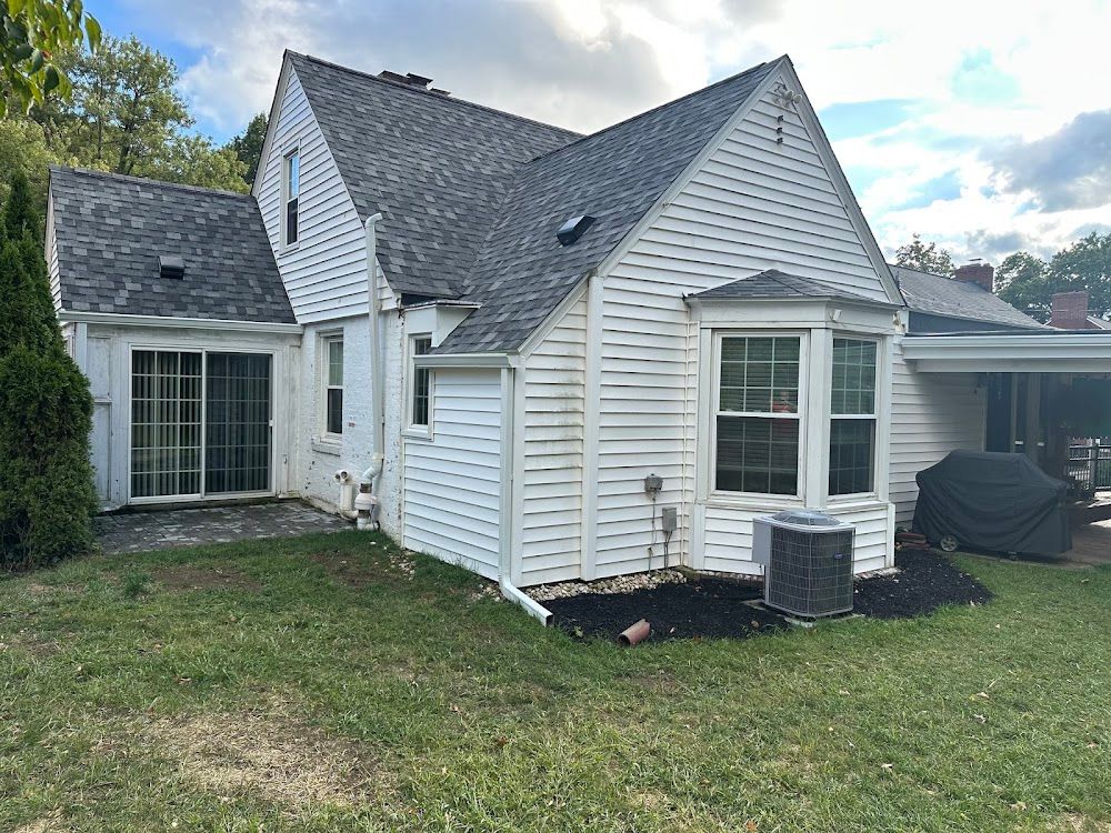 White house exterior with sliding glass door, bay window, and air conditioning unit. Gray roof, green lawn.