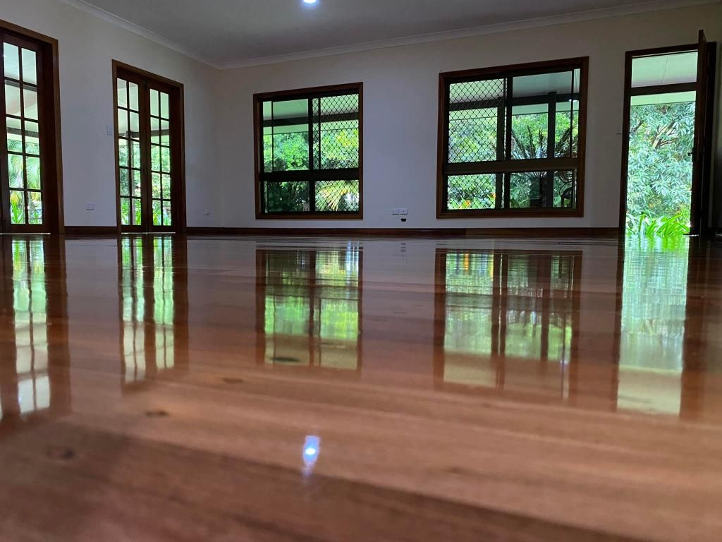 A Large Empty Room With A Wooden Floor And Lots Of Windows — AJ's Cleaning & Floor Sanding In Woree, QLD