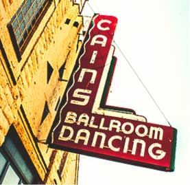 A red sign that says ballroom dancing hangs from the side of a building