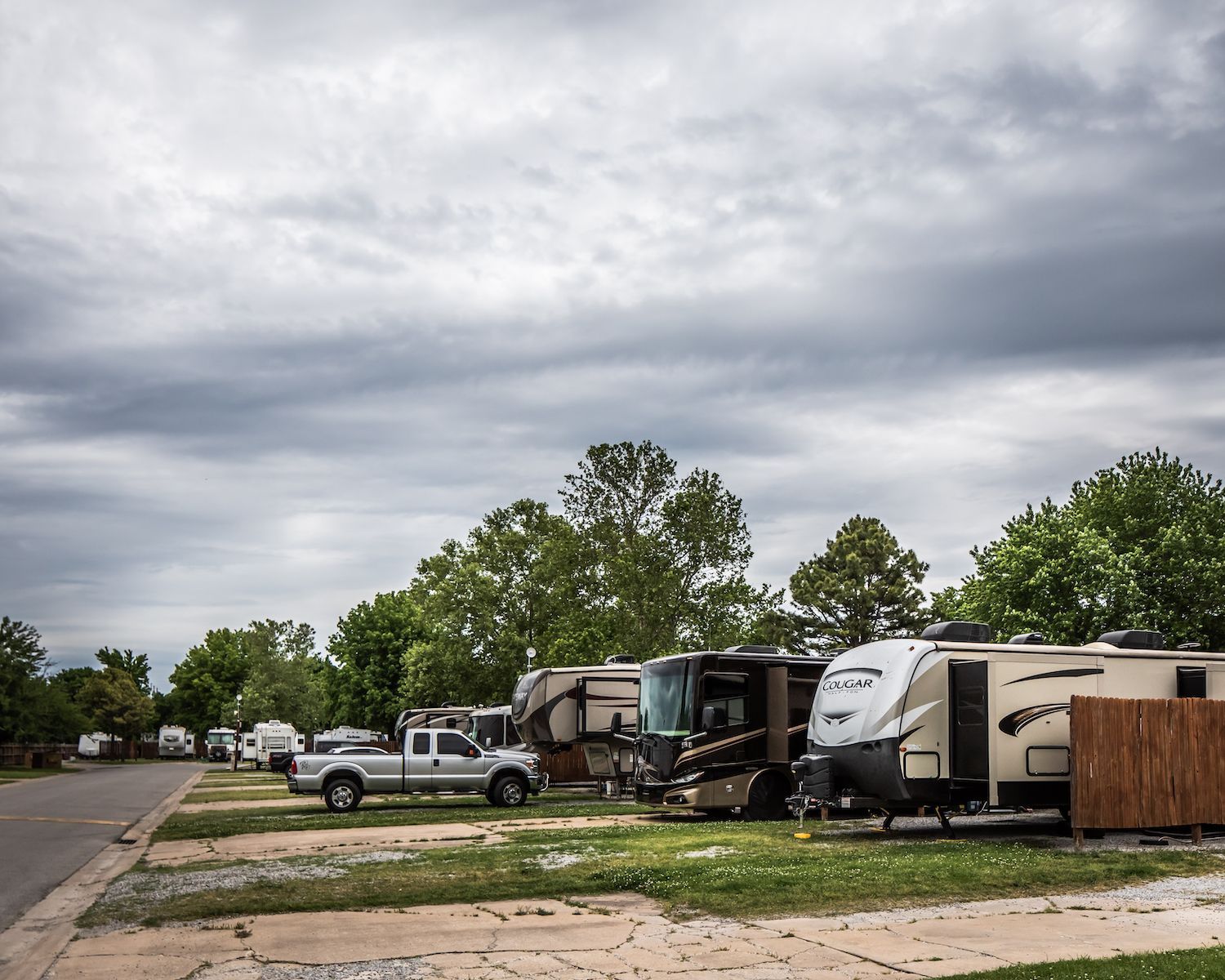 A row of rv 's are parked in a lot on a cloudy day.