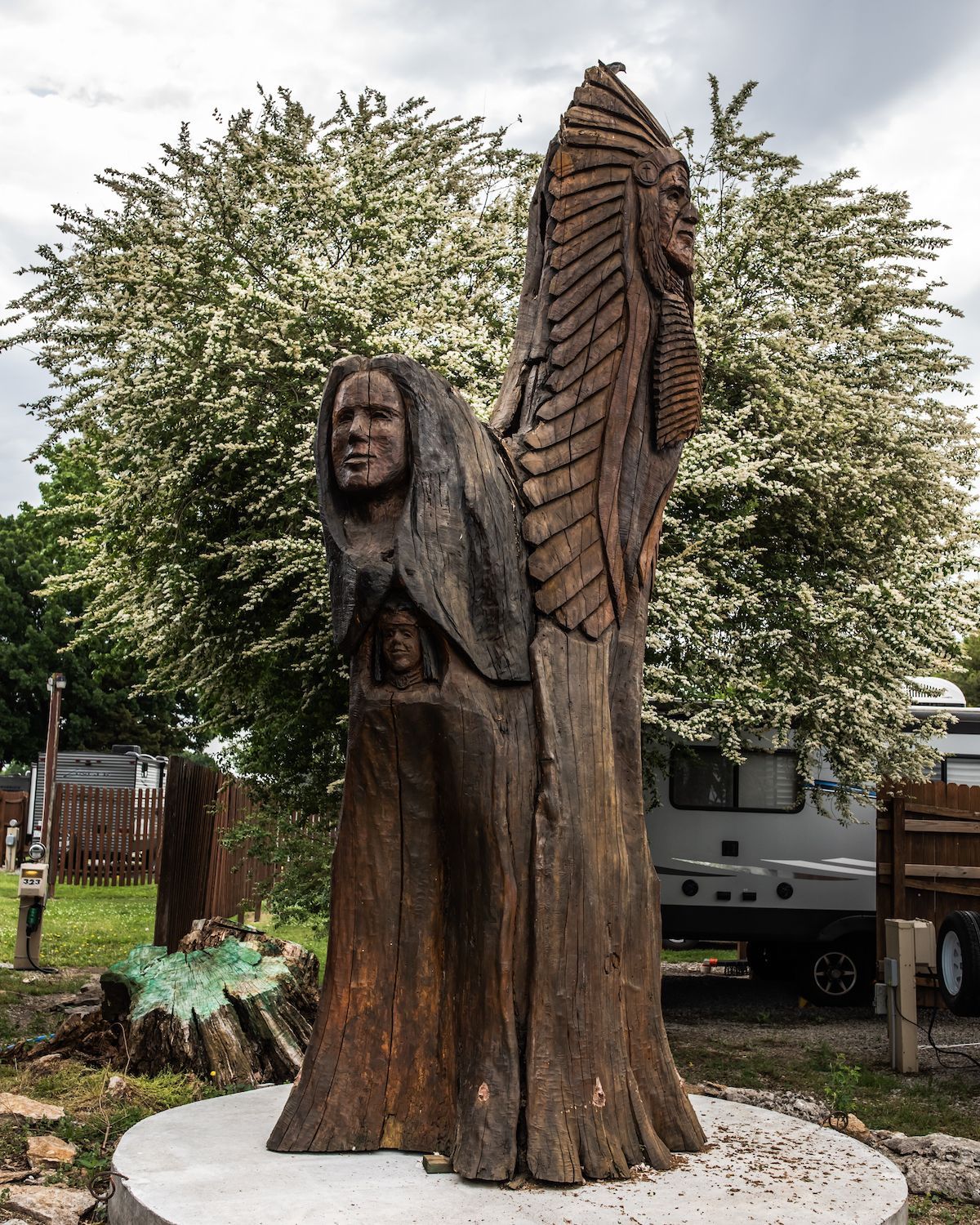 A wooden statue of a man standing next to a tree stump.