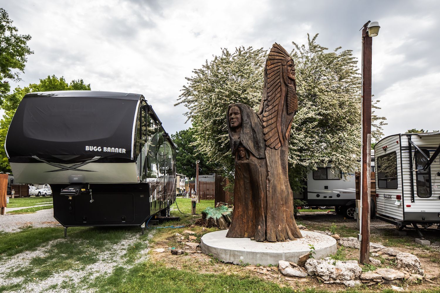 A statue of a woman is carved into a tree stump in front of a trailer.