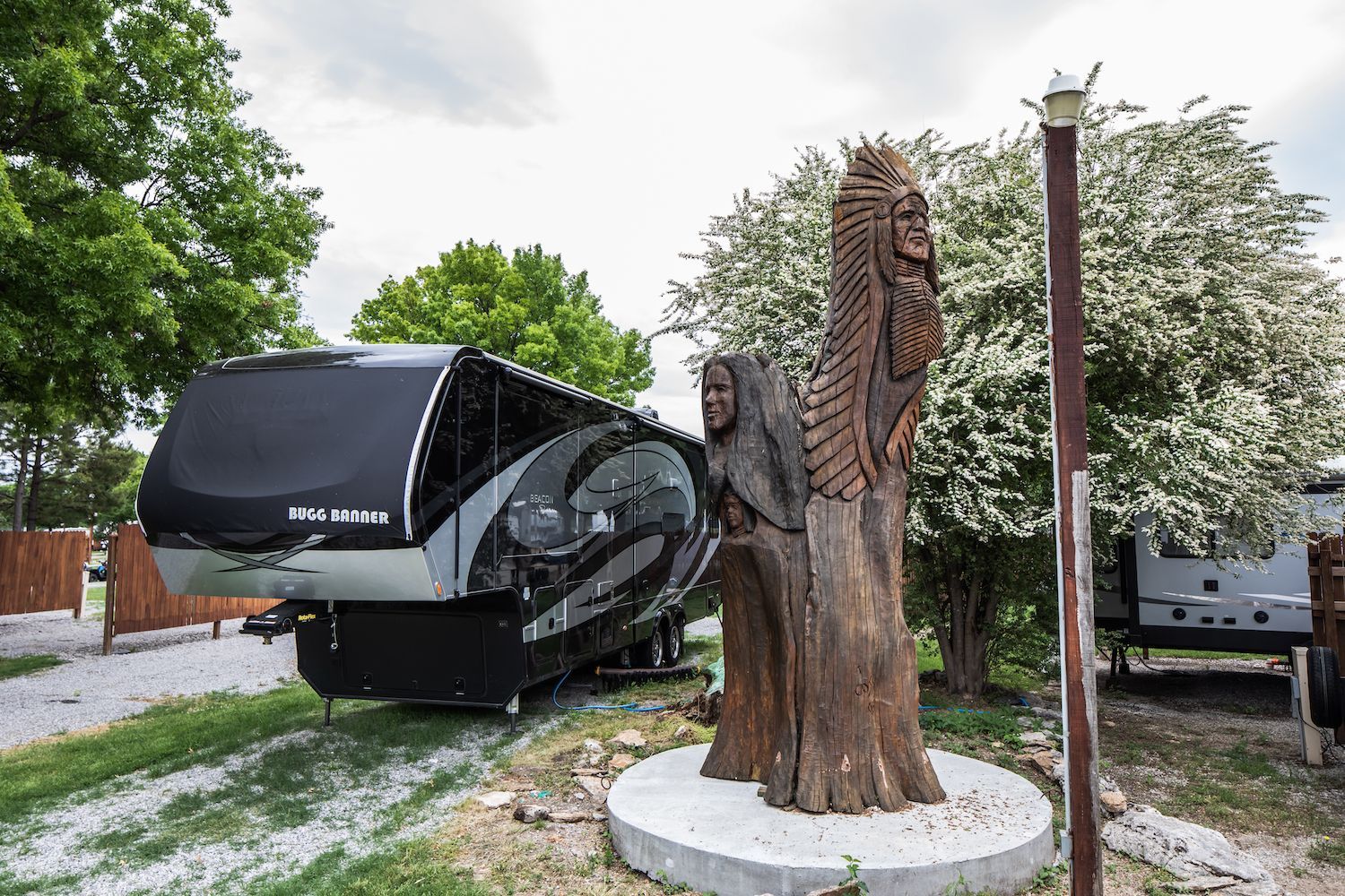 A rv is parked next to a statue of two people carved into a tree.
