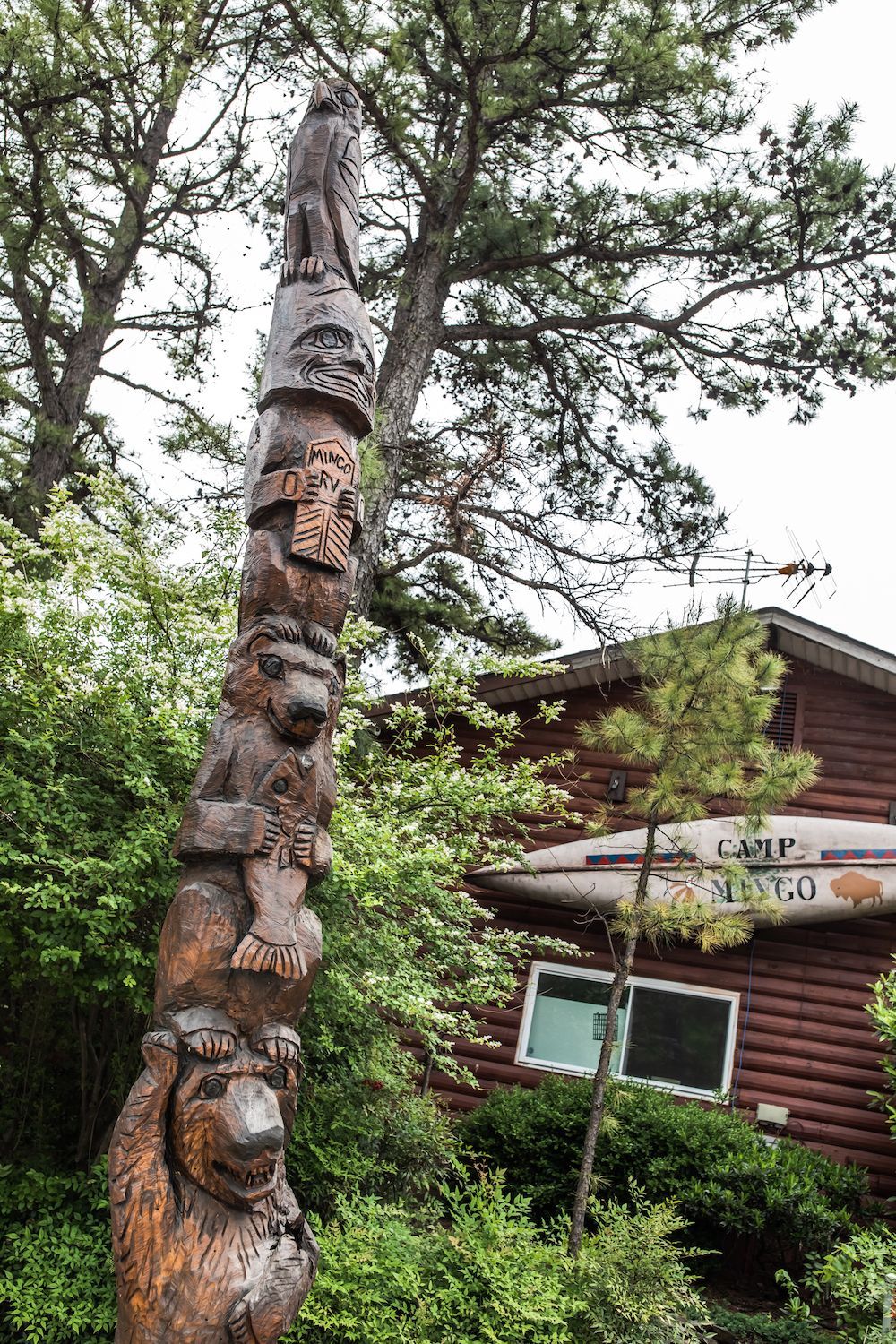 A wooden totem pole is in front of a log cabin.
