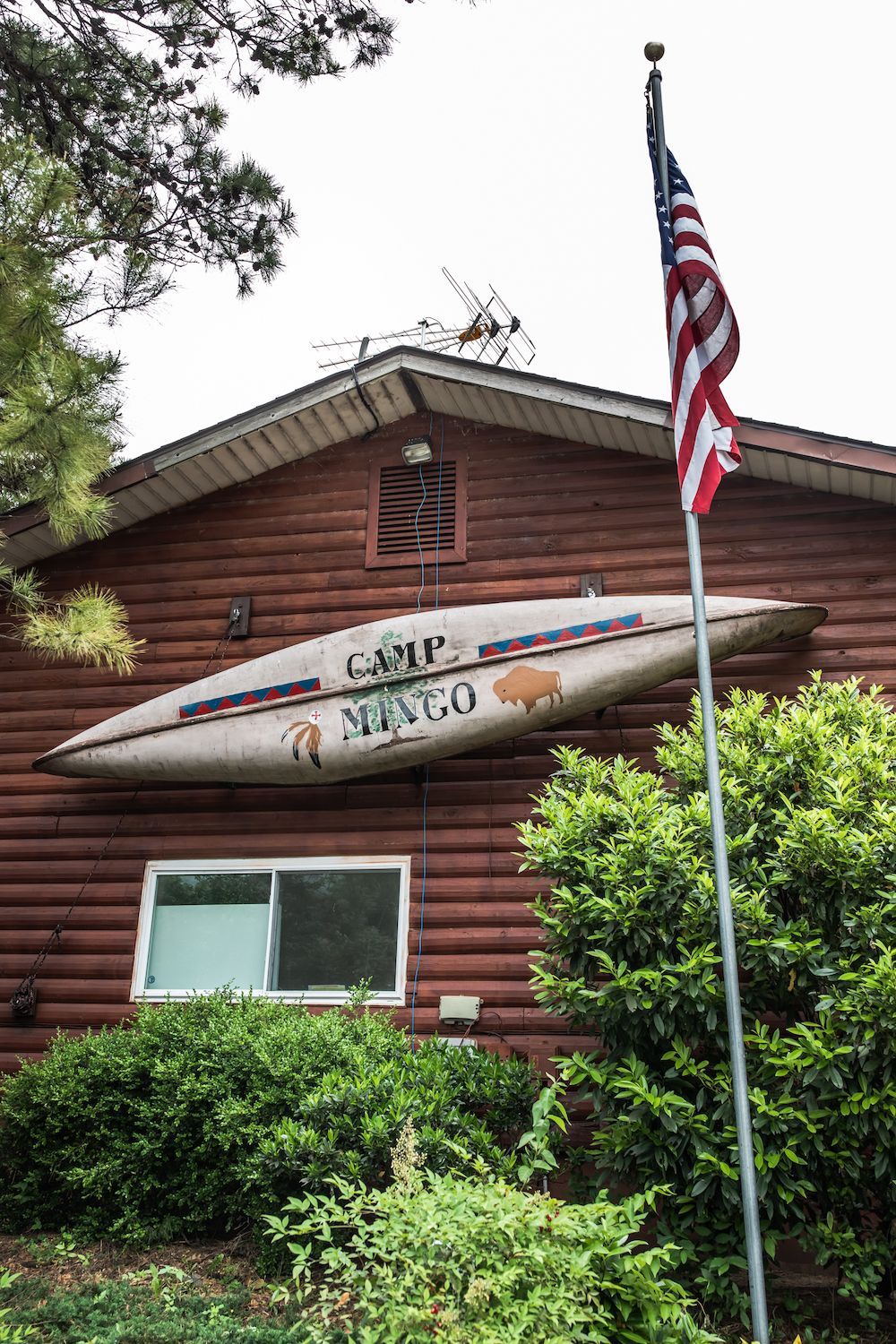 A large kayak is hanging on the side of a log cabin.