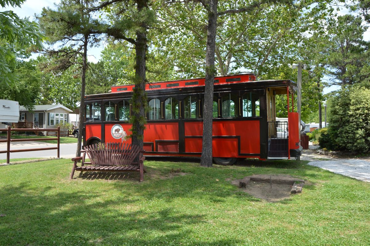 A red bus is parked in a grassy area surrounded by trees.