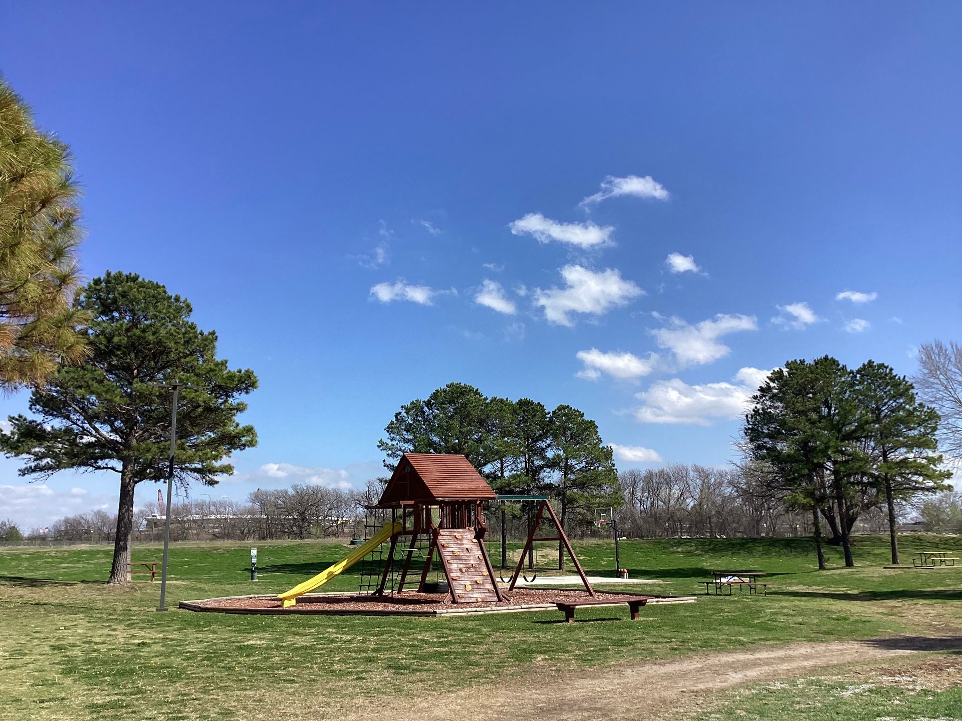 A playground in a park with trees and a blue sky in the background.