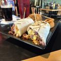 Tray of wraps and fries on a restaurant table with a drink in the background