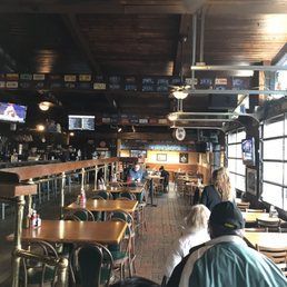 Rustic bar interior with wood tables, TVs, and a few patrons seated at the counter and tables