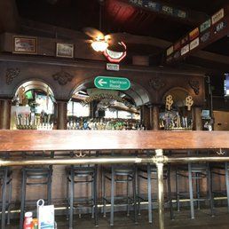 Empty pub bar with stools, wood counter, arched mirrors, and a green direction sign overhead.
