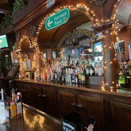 Cozy bar interior with bottle-lined wooden counter, warm string lights, and Hamilton Road sign above mirror